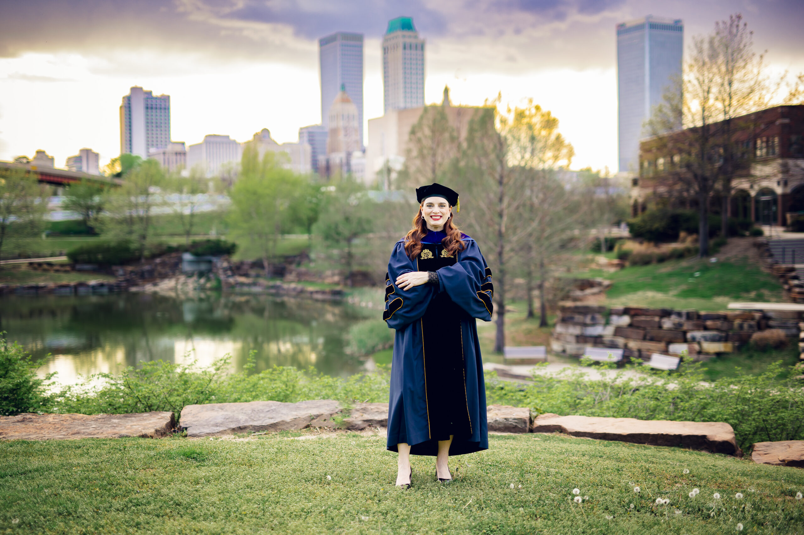 Megan Weinkauf in PhD regalia standing in a park overlooking downtown Tulsa.